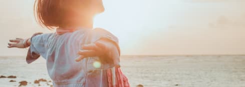 Woman next to a body of water with her arms outstretched, basking in the sun.