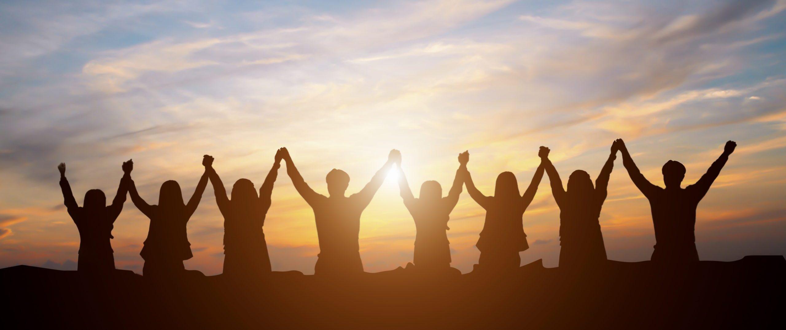 Young professionals holding hands and seated facing a sunset