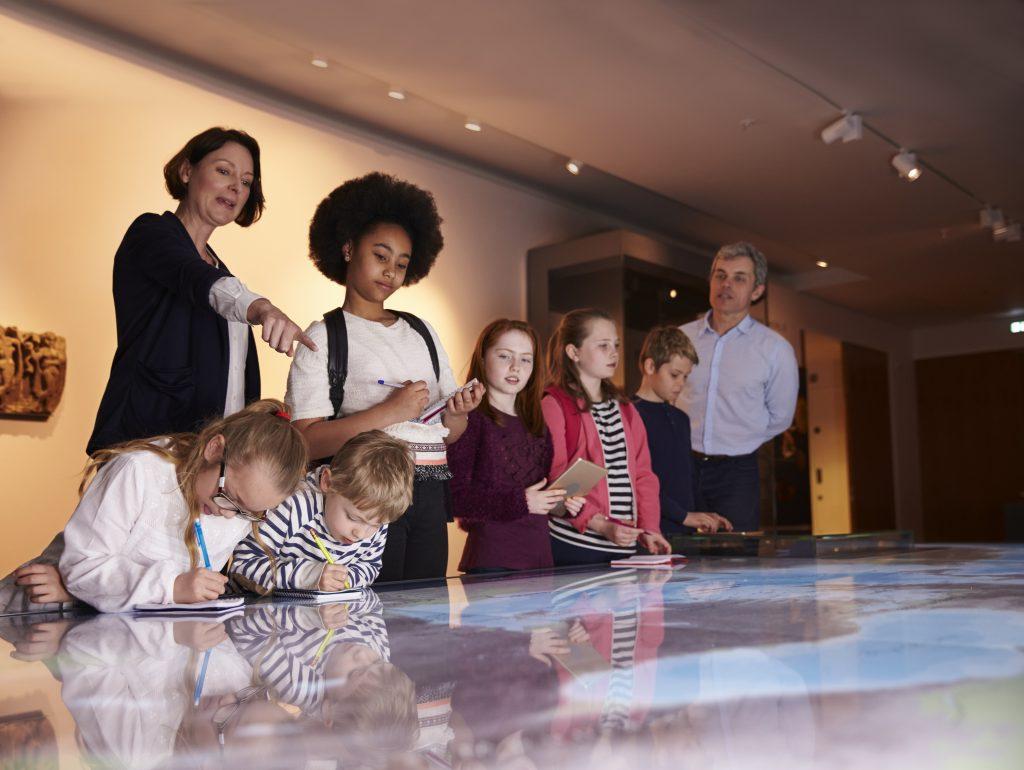 Pupils On Trip To Museum Looking At Map And Making Notes