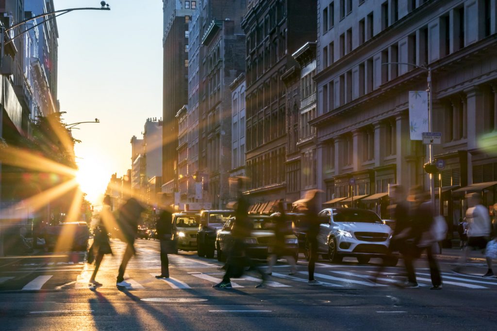 Rays of sunlight shine on the busy people walking across an intersection in Midtown Manhattan in New York City NYC.